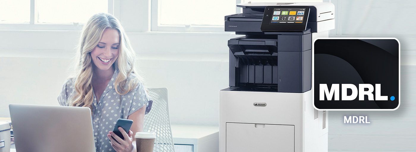 Smiling woman working at a computer and mobile phone next to a Xerox printer