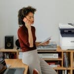 Xerox® C325 Colour Multifunction Printer in a home office environment A woman sitting at a desk having a call next to a Xerox® C325 Printer